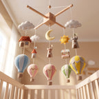 Handmade felt baby mobile featuring colorful hot air balloons, castles, a moon, and sun hanging over a wooden baby crib, adventure-themed nursery decor