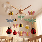 Handmade felt baby mobile featuring colorful bees, butterflies, dragonflies, and ladybugs hanging over a wooden baby crib, insect-themed nursery decor.
