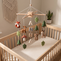 Handmade personalized felt baby mobile featuring forest animals, pine trees, and leaves, with the name 'ANNA' hanging over a wooden baby crib, woodland nursery decor