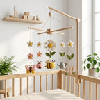 Handmade felt bee garden baby mobile with daisy flowers, butterfly, ladybug, watering can, and garden fence hanging above a wooden crib.