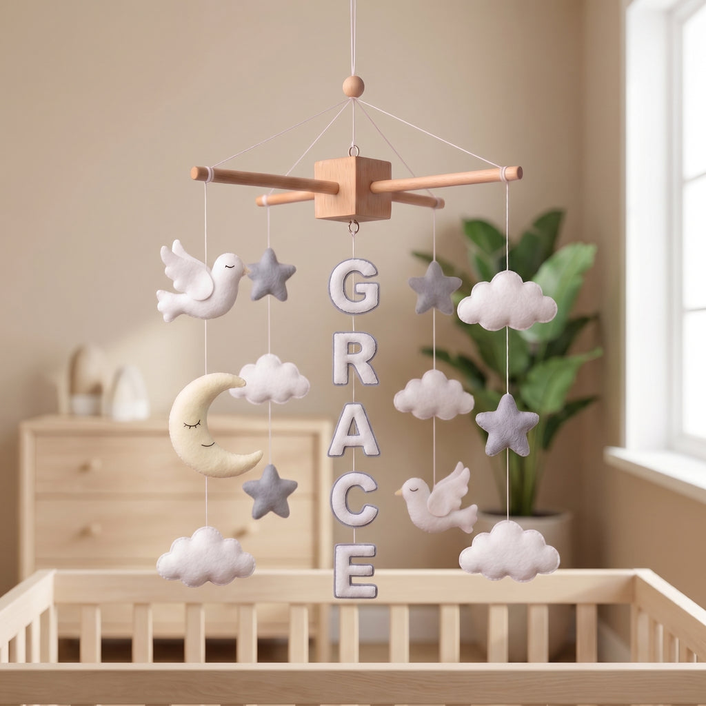 Handmade personalized felt baby mobile with peace doves, clouds, stars, and a crescent moon, featuring the name 'GRACE' hanging over a wooden baby crib, peaceful nursery decor