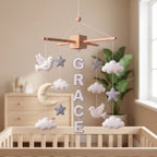 Handmade personalized felt baby mobile with peace doves, clouds, stars, and a crescent moon, featuring the name 'GRACE' hanging over a wooden baby crib, peaceful nursery decor