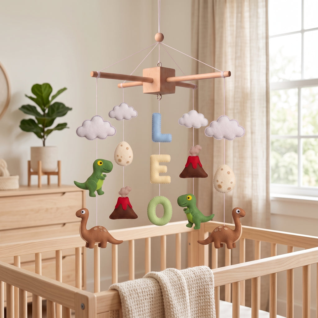 Handmade personalized felt baby mobile featuring dinosaurs, dinosaur eggs, and volcanoes, with the name 'LEO' hanging over a wooden baby crib, prehistoric-themed nursery decor