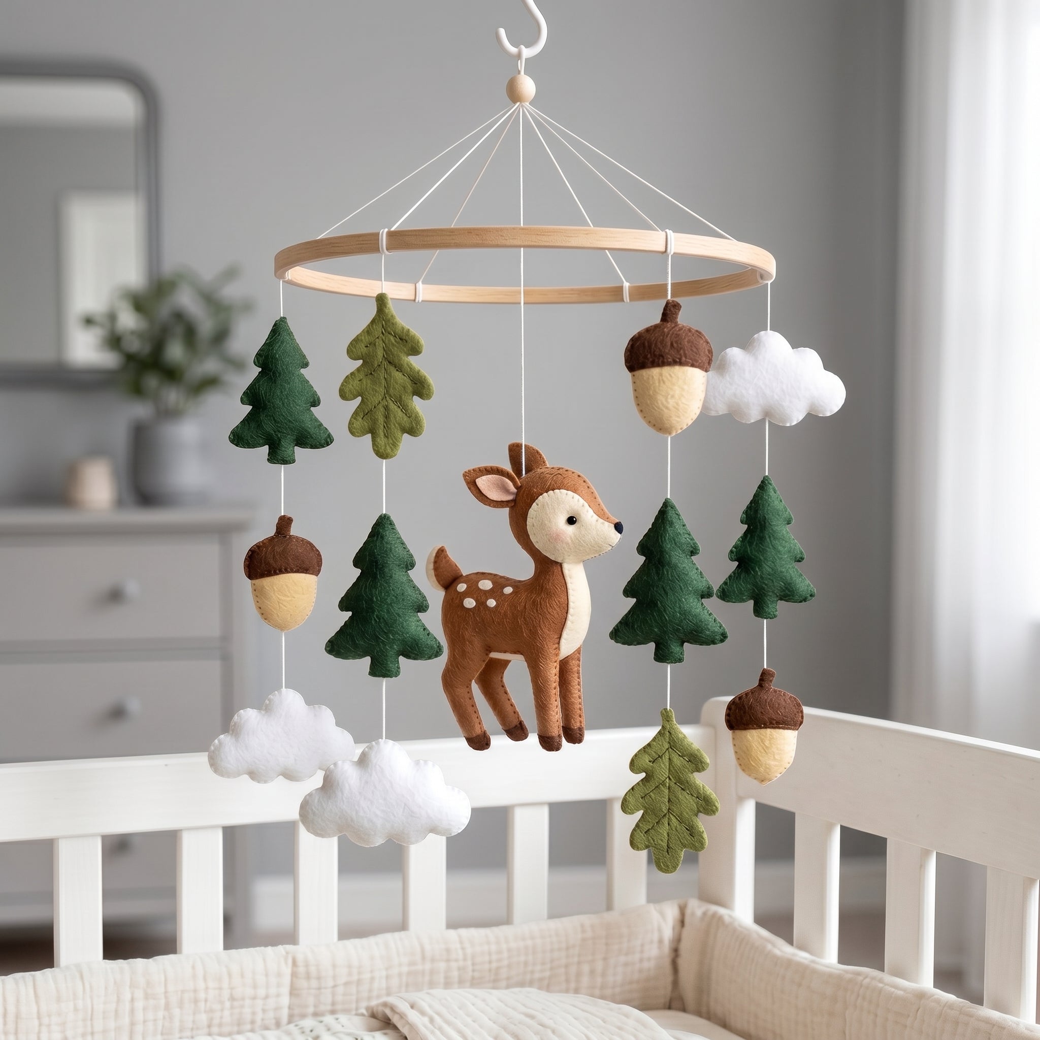 Handmade felt baby mobile featuring a central deer, surrounded by pine trees, oak leaves, acorns, and clouds hanging from a circular wooden frame over a baby crib, rustic forest nursery decor
