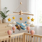 Handmade felt airplane baby mobile with hot air balloons, clouds and stars hanging above a wooden crib.