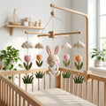 Handmade felt bunny baby mobile with tulips, clouds and grass hanging above a wooden crib in a spring nursery.