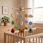 Handmade felt baby mobile featuring various insects, a chrysalis, flowers, and weather elements hanging over a wooden baby crib, nature and life cycle themed nursery decor