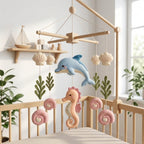 Handmade felt ocean baby mobile with a dolphin, seahorse, seashells and seaweed hanging above a wooden crib.