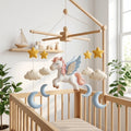 Handmade felt Pegasus baby mobile with clouds, stars and crescent moons hanging above a wooden crib in a dreamy nursery.