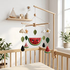 Handmade felt watermelon baby mobile with leaves, flowers and watermelon slices hanging above a wooden crib.