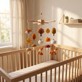 Handmade felt baby mobile featuring foxes, pumpkins, mushrooms, and autumn leaves hanging over a wooden baby crib, fall woodland themed nursery decor