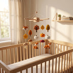 Handmade felt baby mobile featuring foxes, pumpkins, mushrooms, and autumn leaves hanging over a wooden baby crib, fall woodland themed nursery decor