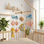 Handmade felt ocean baby mobile with angelfish, seahorse, starfish, coral, seashell, bubbles and seaweed above a wooden crib.