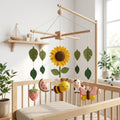 Handmade felt summer baby mobile with bee, sunflower, butterfly, cow, strawberry and watermelon hanging above a wooden crib.
