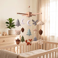 Handmade felt baby mobile featuring woodland animals like a fox and bear, along with trees, pinecones, and a snowflake, hanging over a wooden baby crib, forest-themed nursery decor