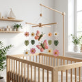 Handmade felt baby mobile featuring butterflies and colorful flowers with tropical leaves hanging from a wooden frame over a wooden baby crib, garden-themed nursery decor.