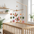Handmade felt baby mobile featuring butterflies and colorful flowers with tropical leaves hanging from a wooden frame over a wooden baby crib, garden-themed nursery decor.
