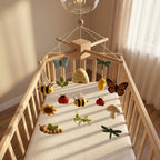 Handmade felt baby mobile featuring various garden insects, bees, butterflies, and flowers hanging over a wooden baby crib, nature-themed nursery decor