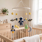 Handmade felt baby mobile featuring an astronaut, rocket ship, planets, and a friendly alien hanging from a circular frame over a wooden baby crib, space-themed nursery decor.