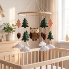 Handmade felt baby mobile featuring a central owl, surrounded by pine trees, oak leaves, and pinecones hanging from a circular wooden frame over a baby crib, rustic forest nursery decor