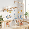 Personalized felt ghost baby mobile with pumpkins, moons, clouds and stars hanging above a wooden crib in a Halloween nursery.