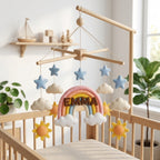 Personalized felt rainbow baby mobile with clouds, stars and suns hanging above a wooden crib in a neutral nursery.