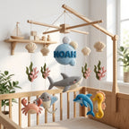 Personalized felt ocean baby mobile with a shark, dolphin, stingray, crab and seahorse hanging above a wooden crib.