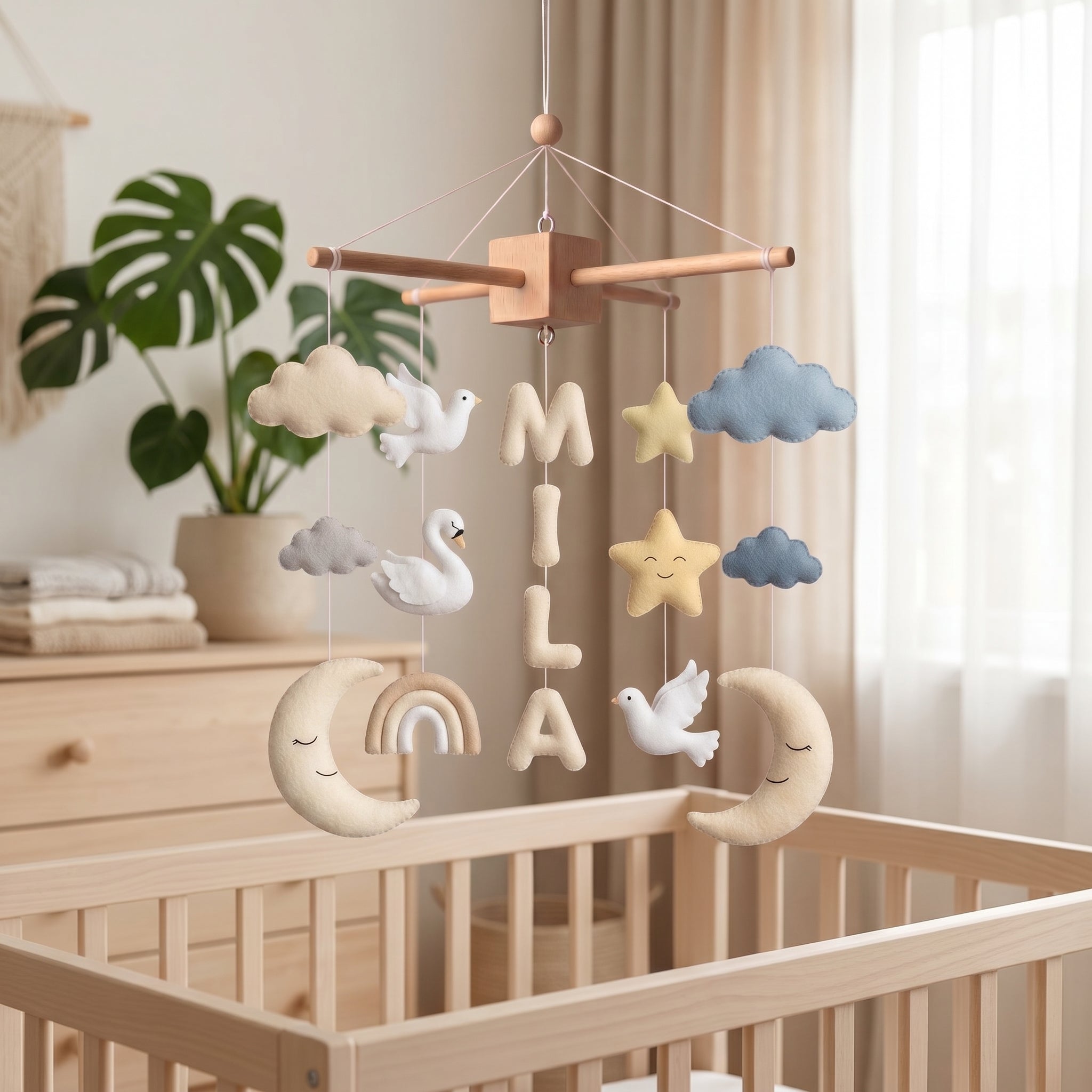 Handmade personalized felt baby mobile with white swans, peace doves, rainbows, and crescent moons, featuring the name 'MILA' hanging over a wooden baby crib, dreamy nursery decor.