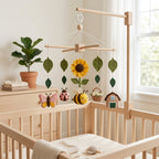 Handmade felt sunflower baby mobile with bee, butterfly, ladybug, flower basket, farmhouse, and green leaves hanging above a wooden crib.