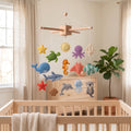 Handmade felt baby mobile featuring a variety of colorful ocean animals including a whale, turtle, shark, starfish, and jellyfish hanging over a wooden baby crib, nautical nursery decor
