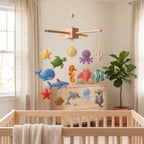 Handmade felt baby mobile featuring a variety of colorful ocean animals including a whale, turtle, shark, starfish, and jellyfish hanging over a wooden baby crib, nautical nursery decor