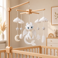 Handmade white dragon felt baby mobile with clouds, stars, moon, snowflake, and feather on a wooden X-frame above a crib.